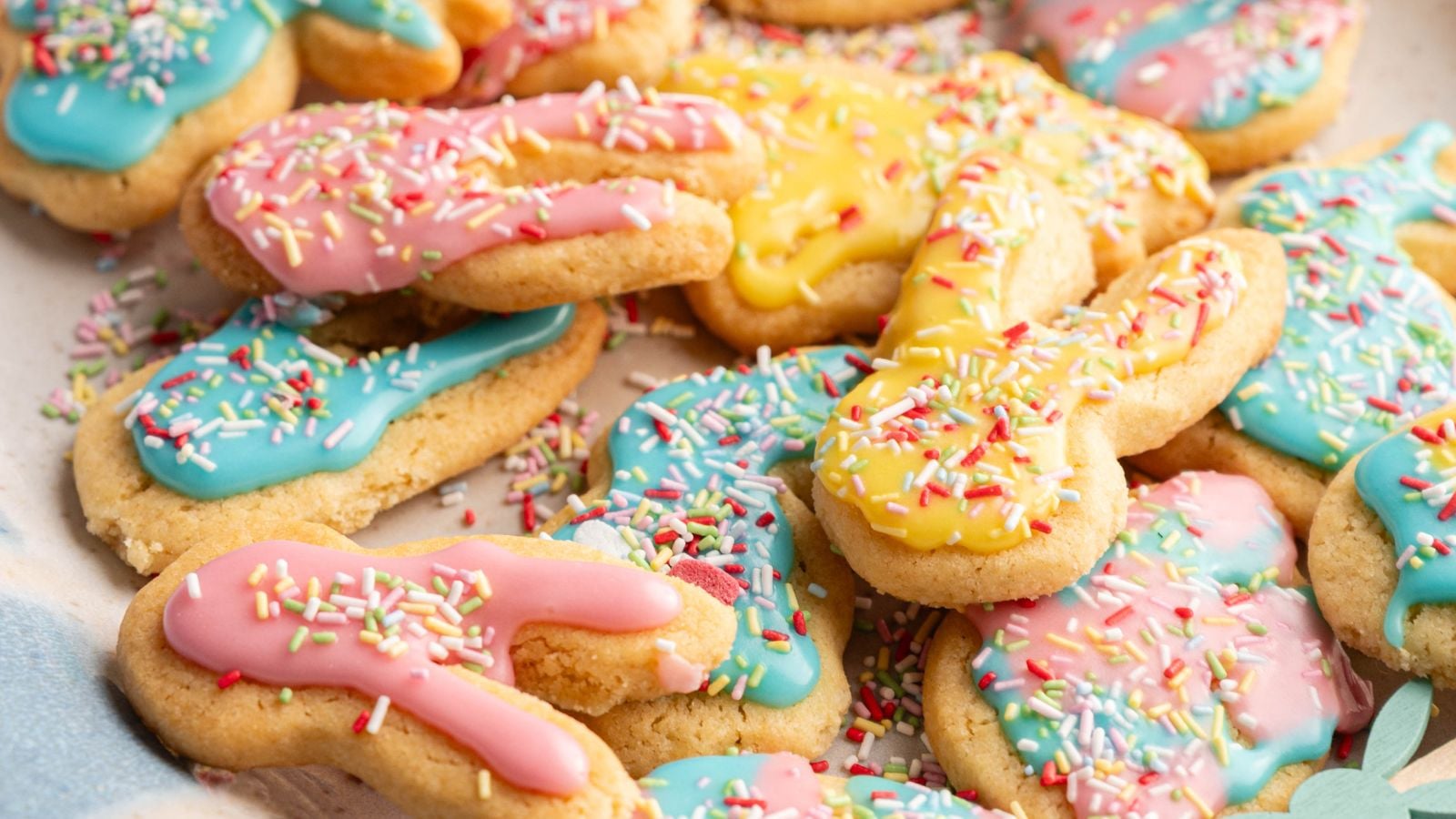 Colorful cookies with pink, blue, and yellow icing and sprinkles are arranged in a pile. The cookies are shaped like bunnies and Easter eggs.