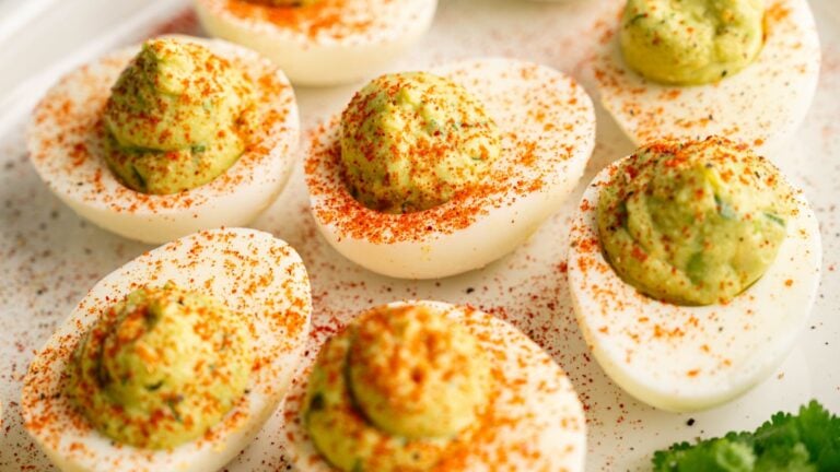 A plate of deviled eggs topped with paprika and garnished with parsley.