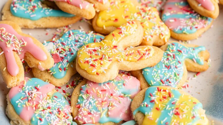 A pile of sugar cookies shaped like bunnies and eggs, decorated with pastel pink, blue, and yellow icing and colorful sprinkles.