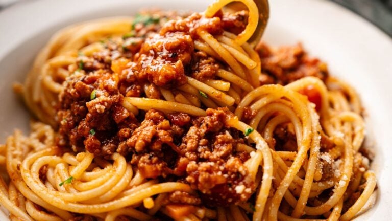 A close-up of spaghetti topped with a chunky meat and tomato sauce, served on a white plate.