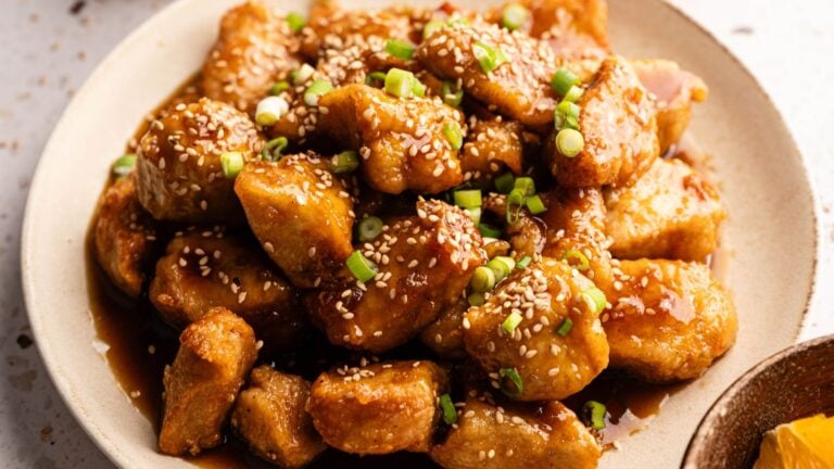 A plate of glazed cooked chicken pieces topped with sesame seeds and chopped green onions.
