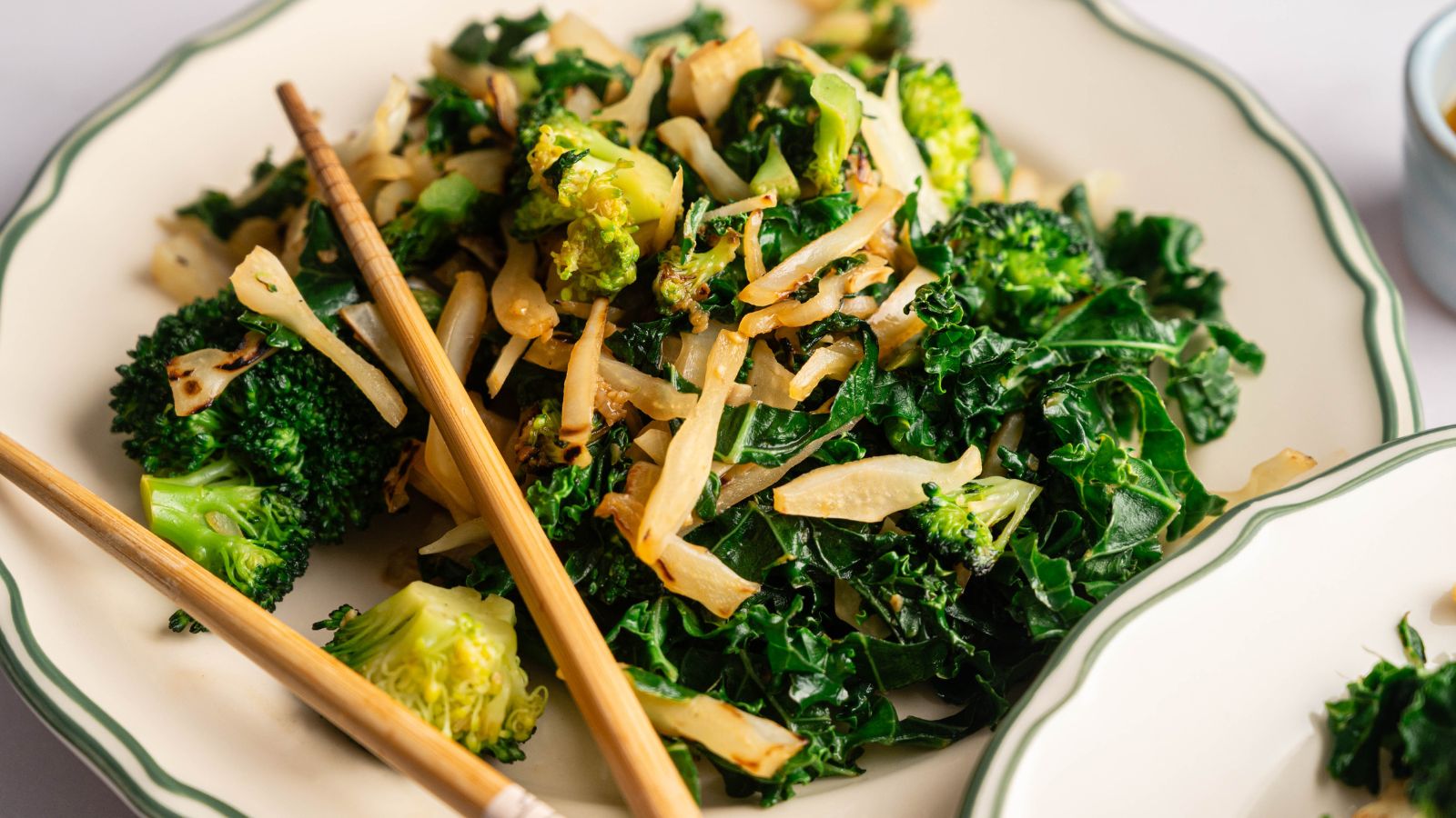 A plate of stir-fried kale, broccoli, and sliced onions, served with a pair of chopsticks on the side.