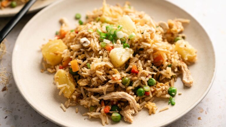 A plate of fried rice with peas, diced carrots, pineapple chunks, shredded chicken, and chopped green onions.