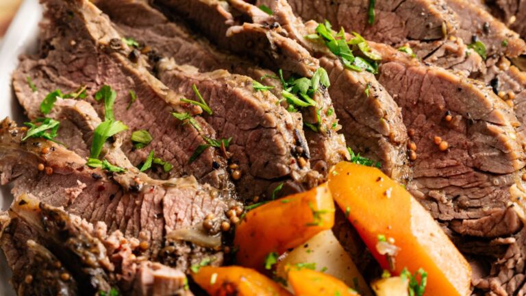 Sliced cooked beef garnished with chopped parsley, served with cooked carrots and potatoes.