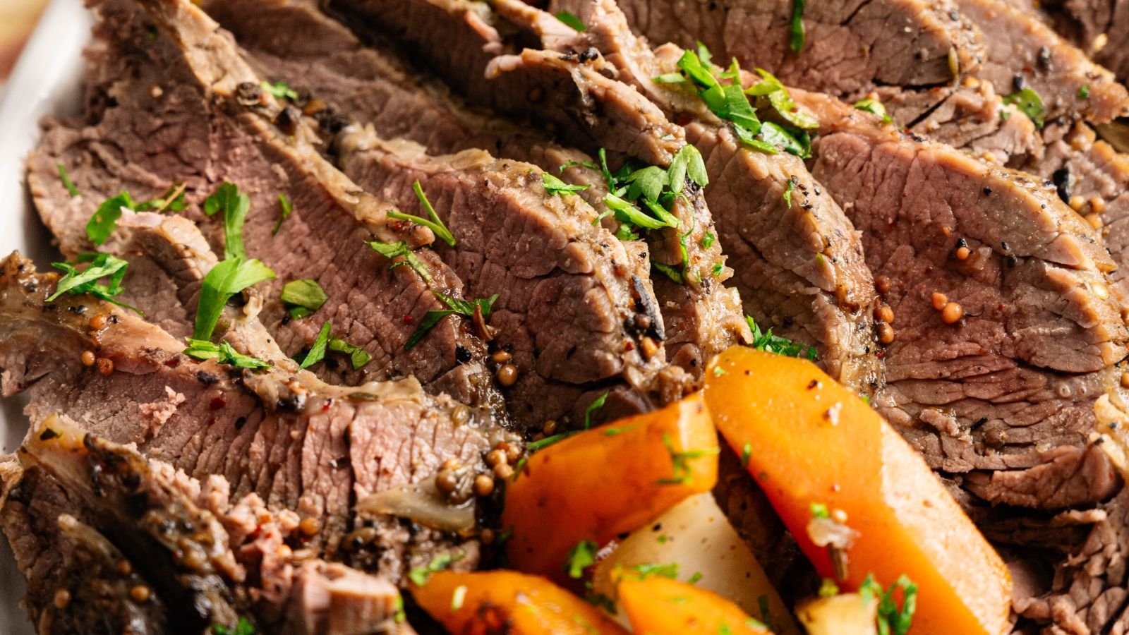 Sliced cooked beef garnished with chopped herbs, served with cooked carrots and potatoes.