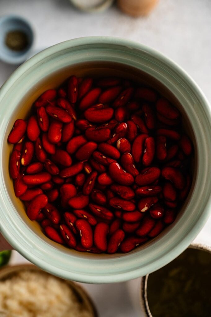 A bowl filled with red kidney beans soaking in water, viewed from above, is the first step in preparing a classic Red Beans and Rice dish.