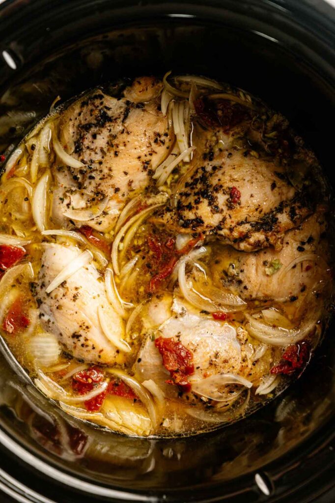 Slow Cooker Chicken Thighs are simmered to perfection with sliced onions, sun-dried tomatoes, hearty seasonings, and savory broth for a flavorful and effortless meal.