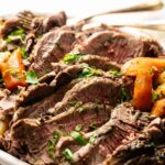 Sliced roast beef garnished with chopped herbs, served with carrots on a white plate—a delicious alternative to Slow Cooker Corned Beef with Cabbage.