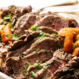 Sliced pot roast beef garnished with chopped herbs, served with cooked carrots on a white plate, reminiscent of a classic Slow Cooker Corned Beef with Cabbage meal.