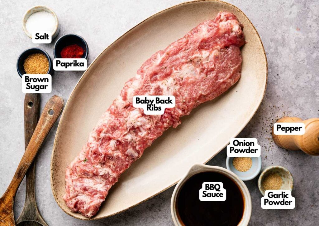 Raw baby back ribs on a platter are surrounded by small bowls of salt, brown sugar, paprika, onion powder, garlic powder, pepper, and a cup of BBQ sauce—perfect for making delicious Slow Cooker Ribs.
