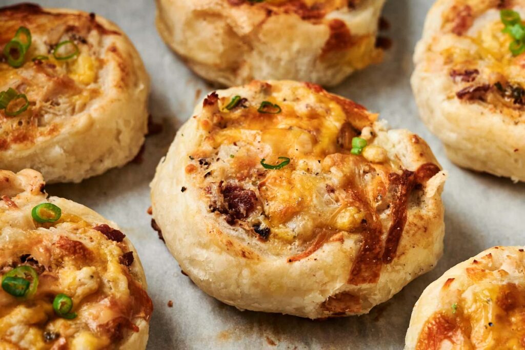 Close-up of Air Fryer Chicken Pinwheels with melted cheese, chopped green onions, and a golden-brown crust on parchment paper.