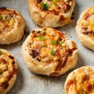 Golden, cheesy, and savory Air Fryer Chicken Pinwheels with bits of bacon and chopped green onions, arranged on a parchment-lined baking sheet.