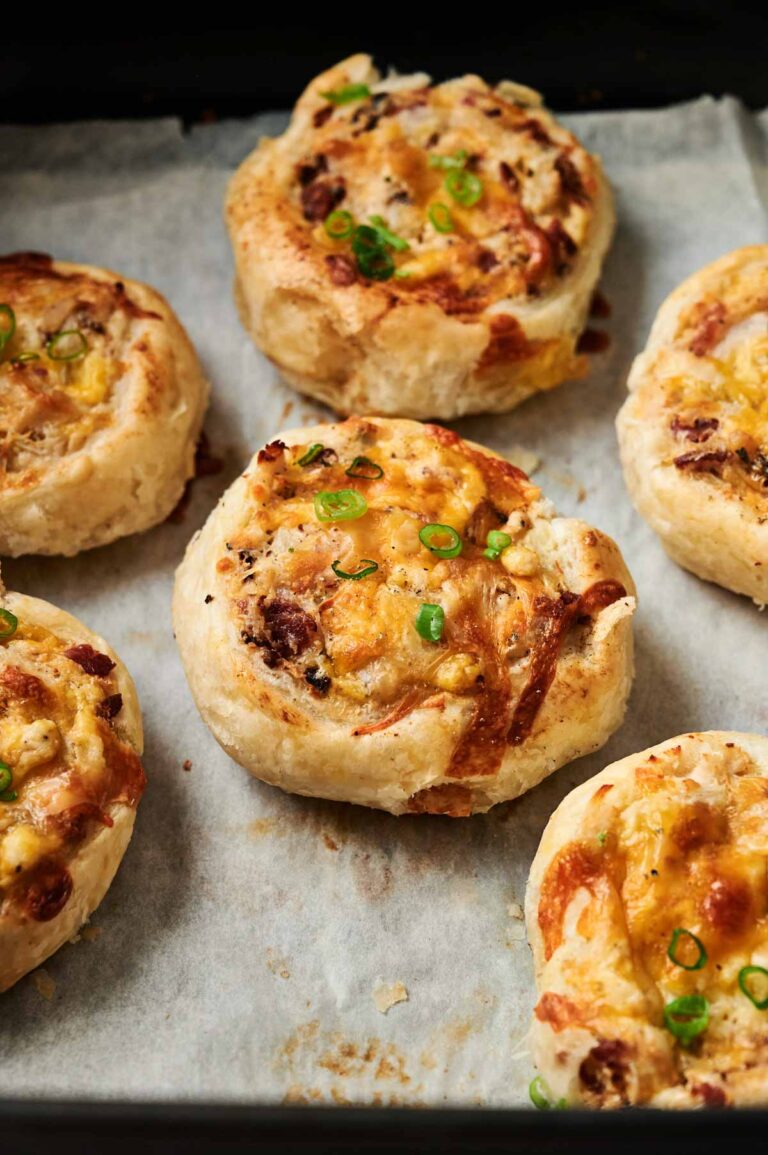 Golden, cheesy, and savory Air Fryer Chicken Pinwheels with bits of bacon and chopped green onions, arranged on a parchment-lined baking sheet.