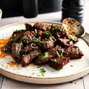 A plate of Air Fryer Garlic Butter Steak Bites garnished with chopped parsley, with a serving spoon resting on the side.