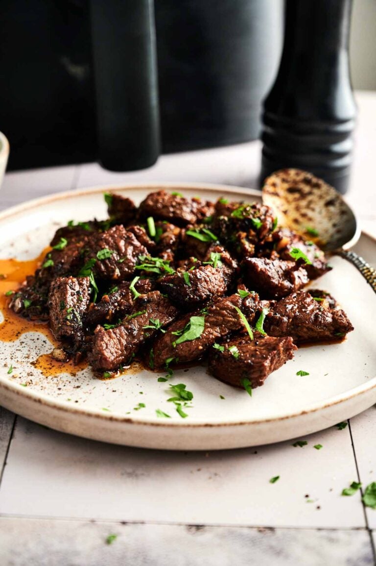 A plate of Air Fryer Garlic Butter Steak Bites garnished with chopped parsley, with a serving spoon resting on the side.