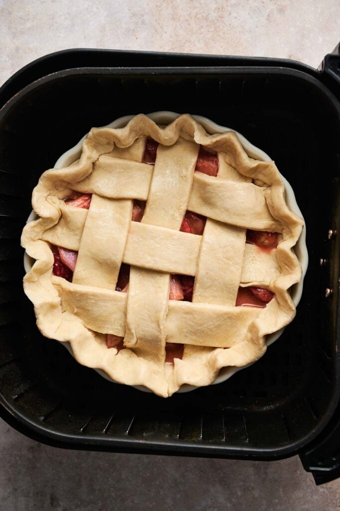 Unbaked lattice-topped Air Fryer Rhubarb Pie placed inside an air fryer basket, ready for baking.