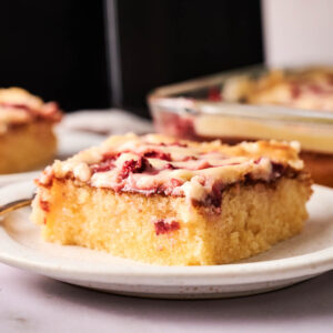 A close-up of a slice of glazed Air Fryer Strawberry Earthquake Cake on a plate, with more cake in the background.