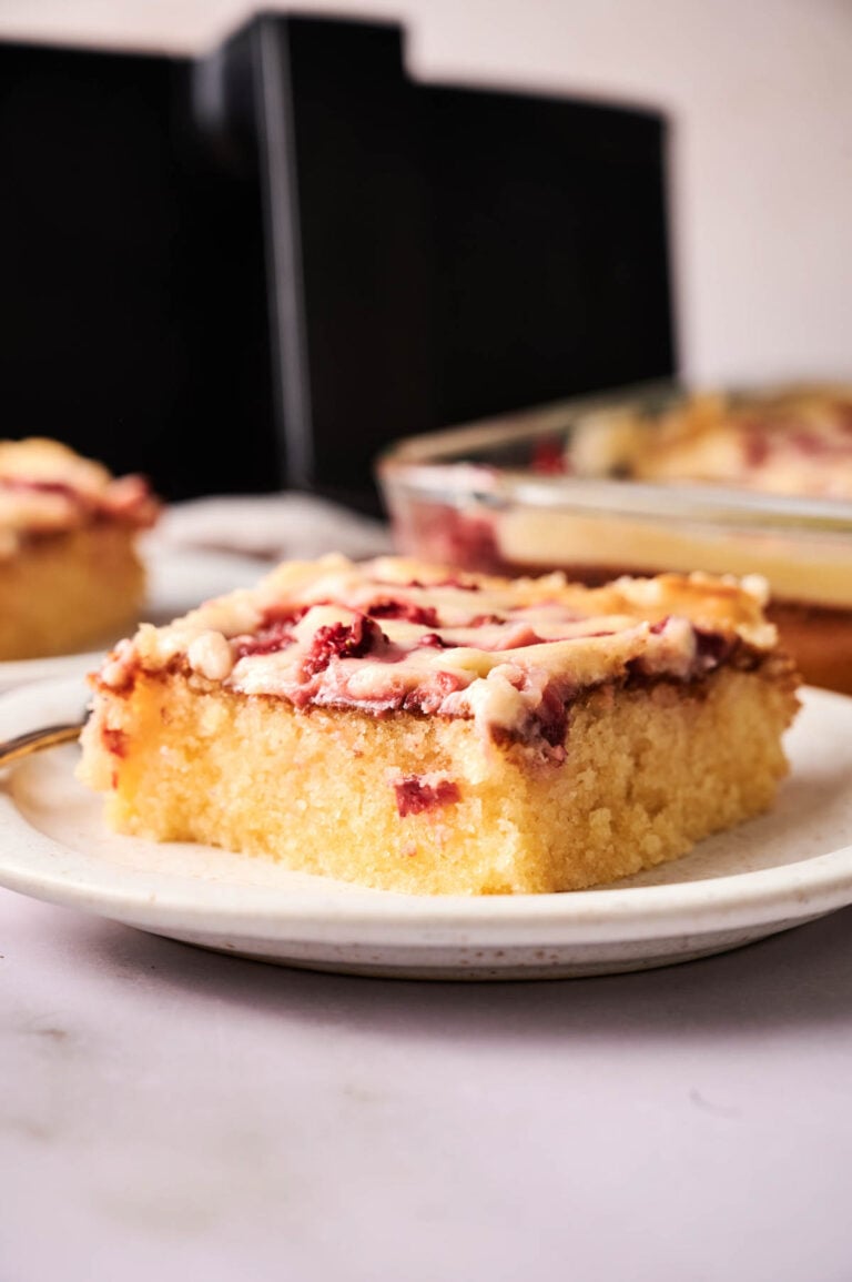 A close-up of a slice of glazed Air Fryer Strawberry Earthquake Cake on a plate, with more cake in the background.
