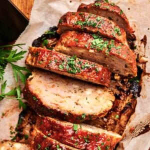 Air Fryer Turkey Meatloaf sliced and garnished with chopped parsley on parchment paper, with a sprig of fresh parsley beside it.