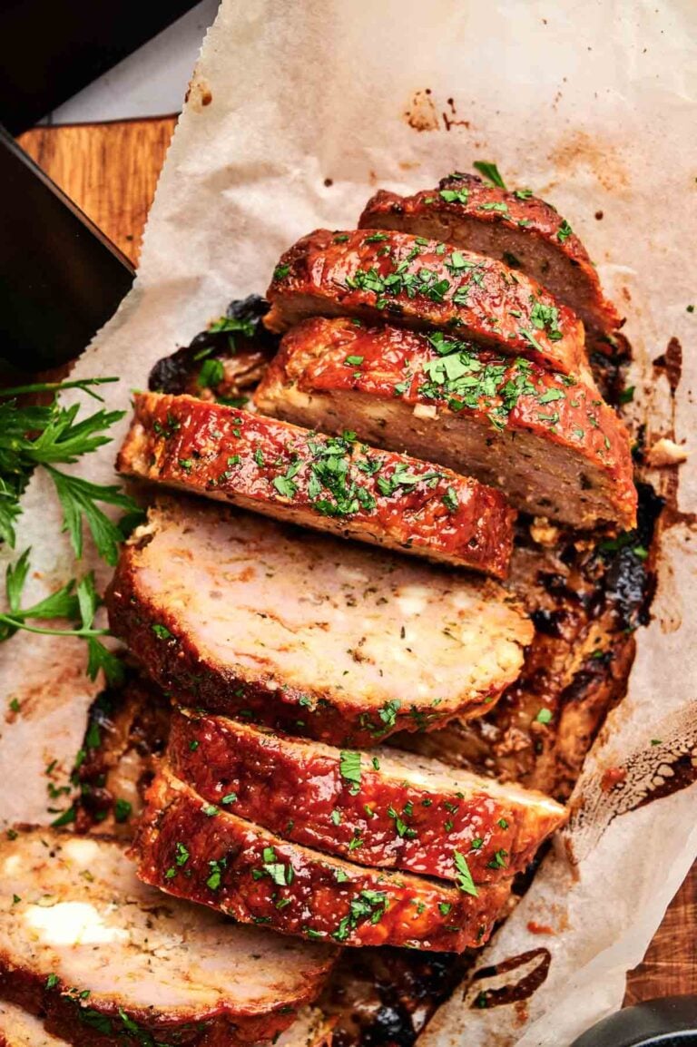 Air Fryer Turkey Meatloaf sliced and garnished with chopped parsley on parchment paper, with a sprig of fresh parsley beside it.