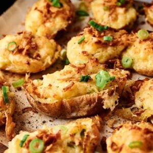 Air Fryer Twice Baked Potatoes&mdash;stuffed potato halves topped with melted cheese, crispy onions, and green onions&mdash;are perfectly arranged on a wooden board for a delicious and convenient twist on a classic favorite.
