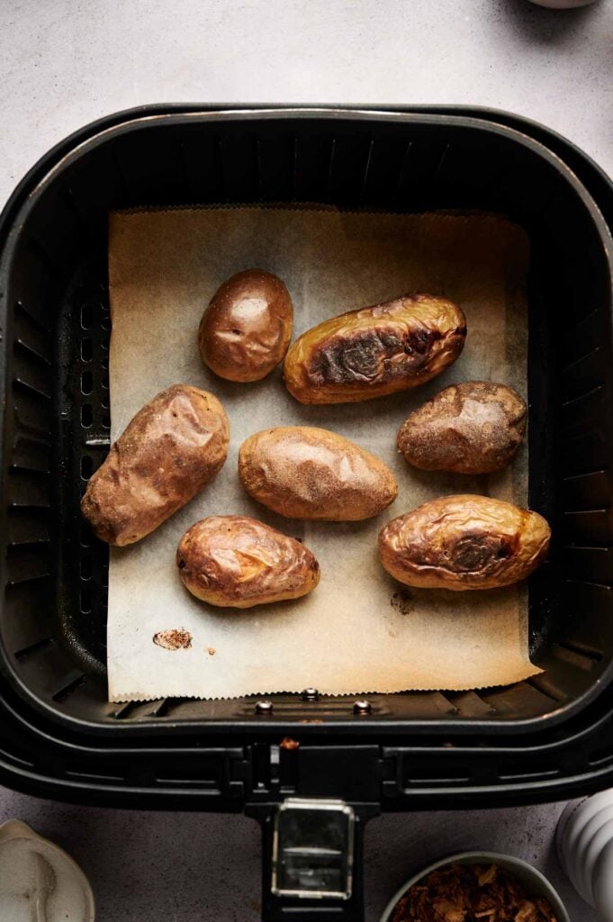 Seven Air Fryer Twice Baked Potatoes rest on parchment paper inside the air fryer basket, perfectly crisp and ready to serve.