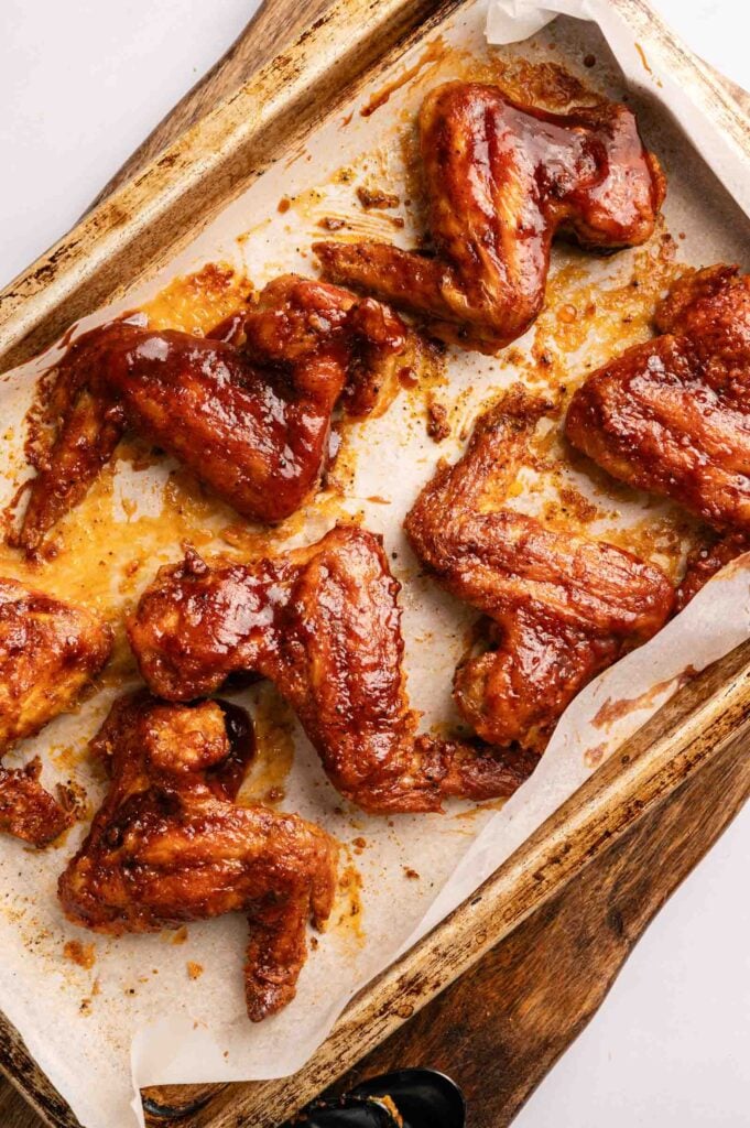 BBQ Wings baked to perfection, coated in a shiny barbecue sauce and arranged on a parchment-lined baking tray with tempting sauce drips visible.