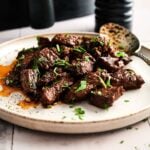 A white plate with Air Fryer Garlic Butter Steak Bites, garnished with chopped herbs and a serving spoon on the side.
