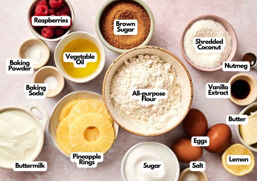 An assortment of labeled baking ingredients on a counter, including flour, sugar, eggs, pineapple rings&mdash;perfect for making an Air Fryer Pineapple Upside Down Cake&mdash;plus raspberries, coconut, buttermilk, butter, spices, lemon, and other baking essentials.