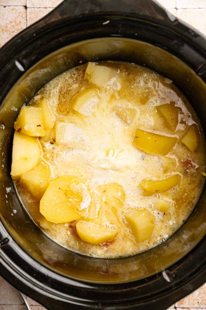 Diced potatoes, butter, and liquid simmer in a slow cooker, forming the base for a creamy Slow Cooker Potato Soup, ready to be mashed.
