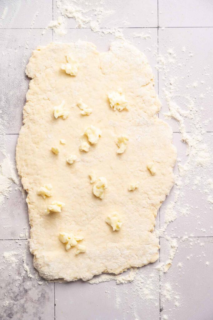 Rolled-out Air Fryer Sourdough Biscuit dough on a floured surface with small dollops of butter scattered on top, ready to be folded or mixed in.