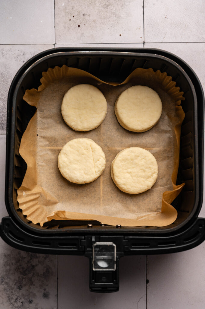 Four round, unbaked Air Fryer Sourdough Biscuits arranged on parchment paper inside an air fryer basket.
