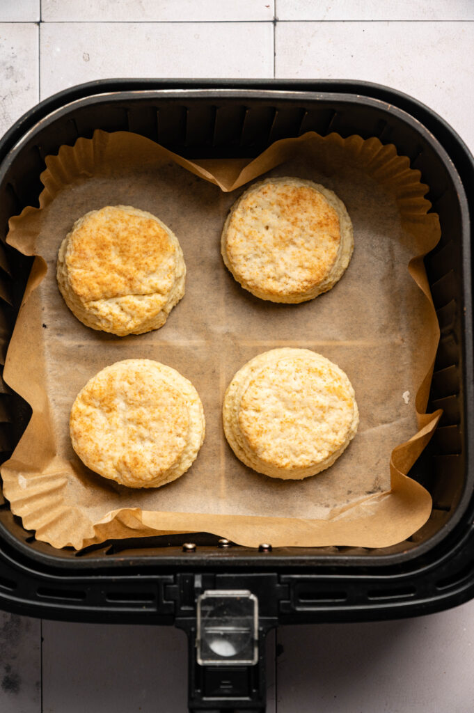 Four Air Fryer Sourdough Biscuits on parchment paper inside an air fryer basket, baked to a light golden brown.