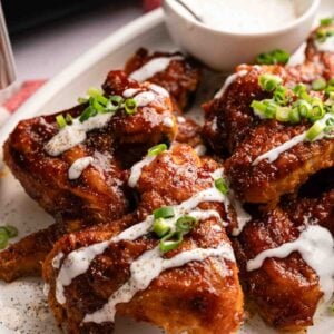 A plate of saucy Air Fryer BBQ Wings garnished with chopped green onions, drizzled with white sauce, and served with a bowl of dip.