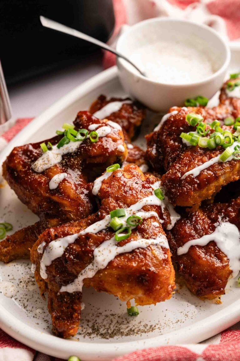 A plate of saucy Air Fryer BBQ Wings garnished with chopped green onions, drizzled with white sauce, and served with a bowl of dip.