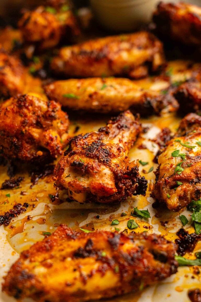 Close-up of crispy Cajun Chicken Wings on a baking sheet, garnished with chopped herbs and surrounded by seasoning and juices.