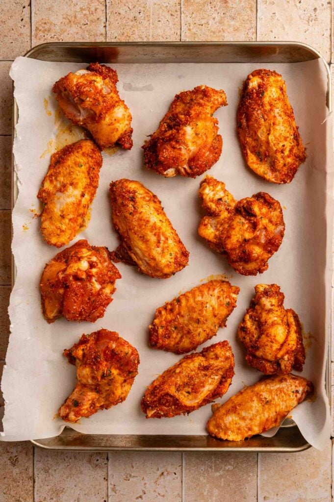 Cajun Chicken Wings arranged on a parchment-lined baking tray, shown from above on a tiled surface.
