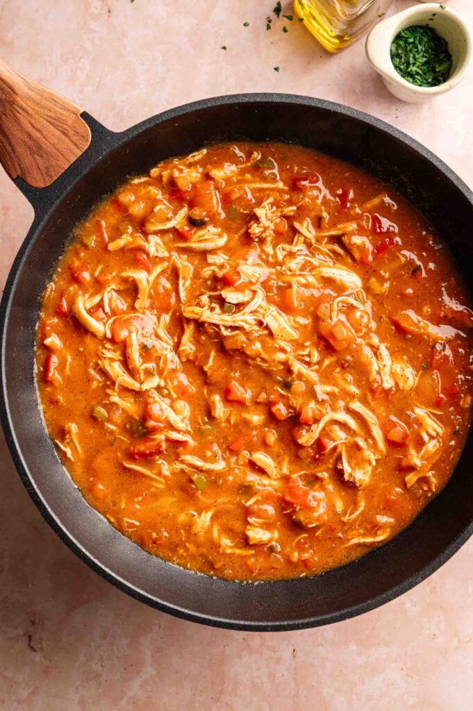 Shredded chicken in a tomato-based sauce simmers in a black skillet on a light-colored countertop, ready to become the star of your next Air Fryer King Ranch Casserole.
