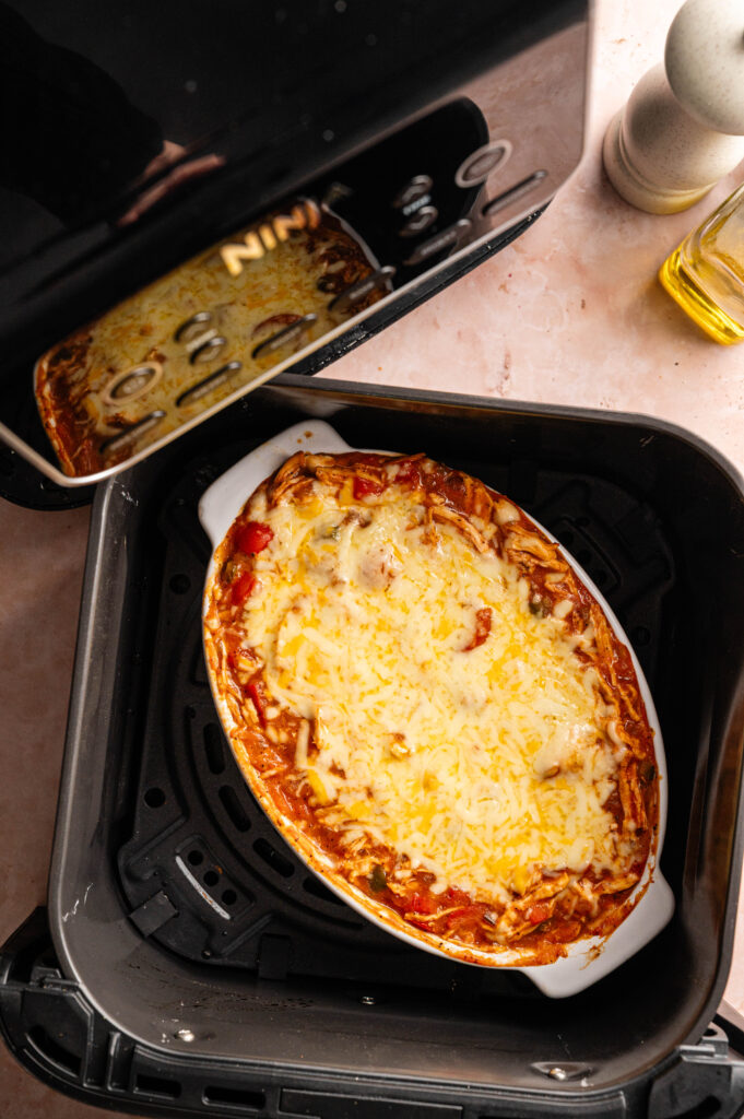 Oval casserole dish filled with cheesy Air Fryer King Ranch Casserole, baked to perfection inside an air fryer, with part of the appliance and countertop visible.