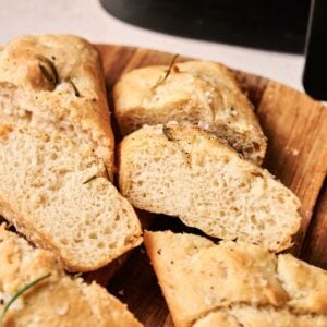 Slices of Air Fryer Focaccia Bread topped with herbs and coarse salt rest on a wooden cutting board.
