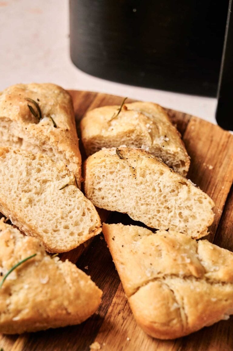 Slices of Air Fryer Focaccia Bread topped with herbs and coarse salt rest on a wooden cutting board.