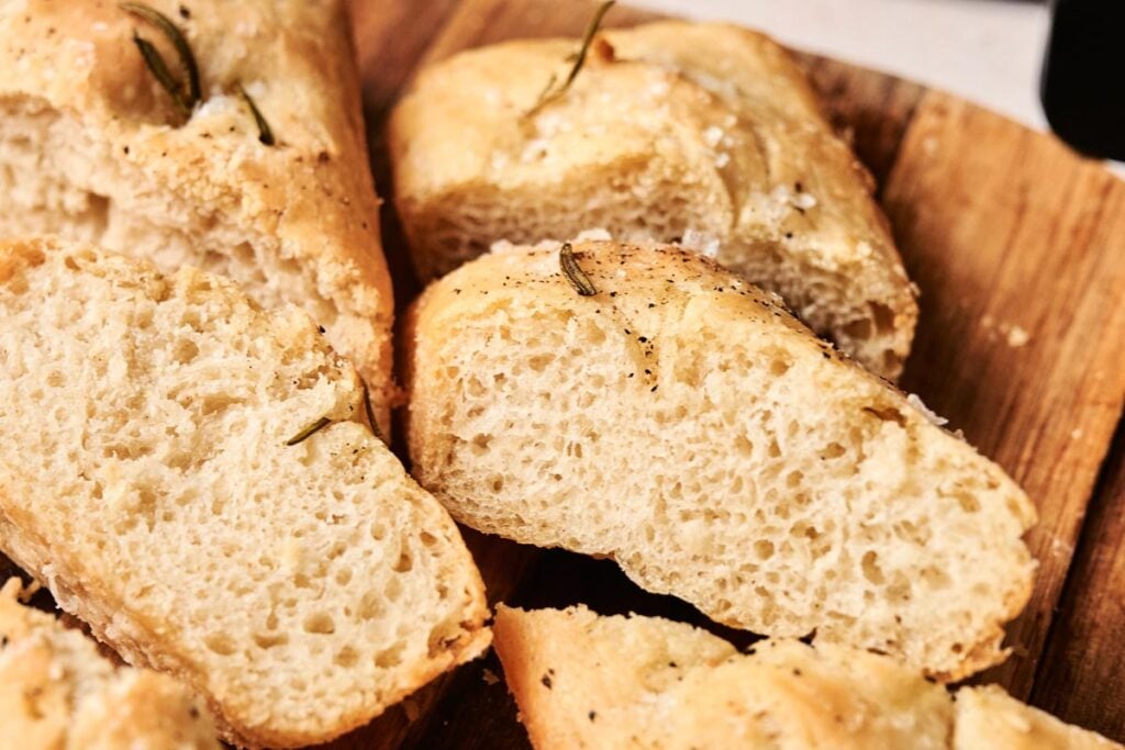 Sliced pieces of Air Fryer Focaccia Bread with a golden crust, sprinkled with salt and rosemary, displayed on a wooden surface.