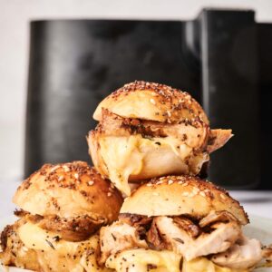 Three sliders on a white plate, with a black air fryer in the background&mdash;perfect inspiration for your next batch of Air Fryer Turkey Sliders.