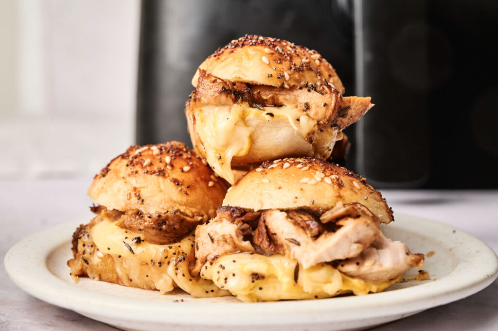 Three sliders with seeded buns are stacked on a white plate, offering a twist on classic Air Fryer Turkey Sliders.