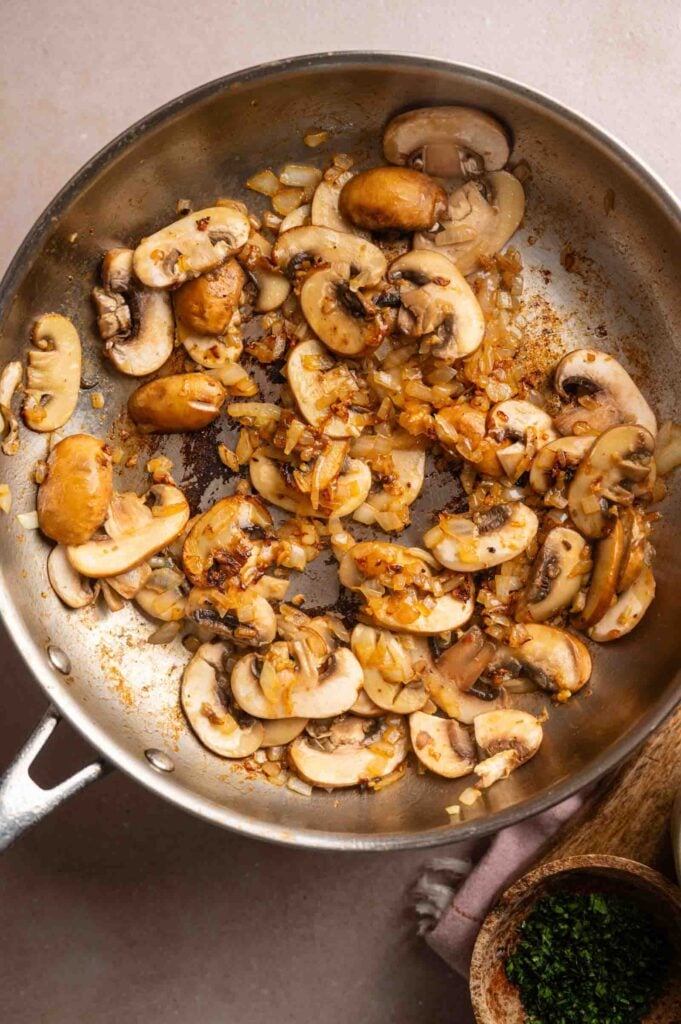 Sliced mushrooms and saut&eacute;ed onions cooking in a stainless steel skillet add rich flavor to Cheesy Chicken Spaghetti Casserole.