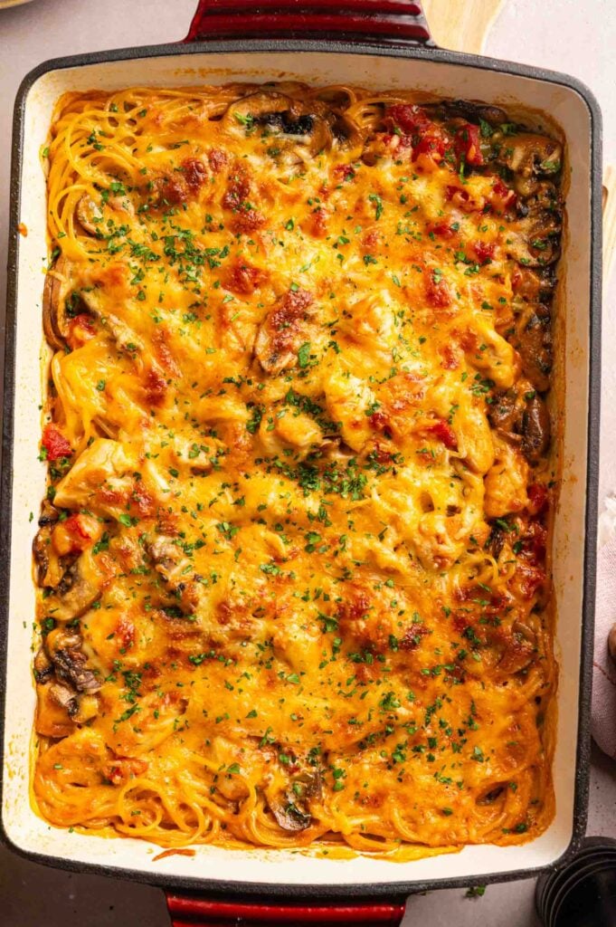 Cheesy Chicken Spaghetti Casserole topped with melted cheese, mushrooms, and herbs, baked to perfection in a rectangular dish.