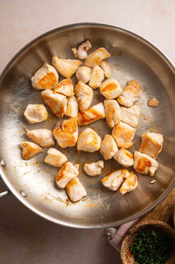 Cubed pieces of chicken breast are being saut&eacute;ed in a stainless steel pan, showing a golden-brown sear&mdash;the perfect start for a flavorful Cheesy Chicken Spaghetti Casserole.
