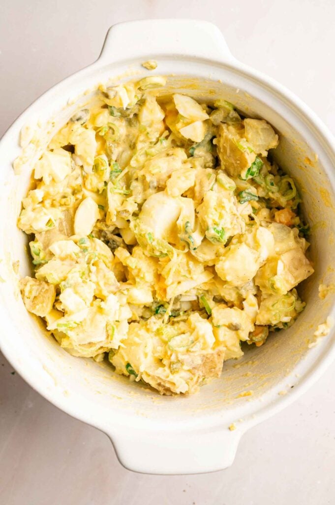 A white bowl filled with creamy Southern Potato Salad, featuring chopped potatoes, hard-boiled eggs, and green onions.