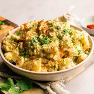 A bowl of Southern Potato Salad garnished with chopped parsley and paprika, placed on a cloth napkin with fresh parsley on the side.