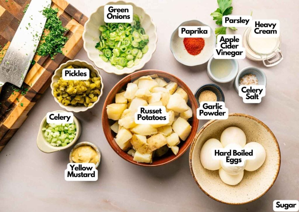 Chopped ingredients for Southern Potato Salad, including russet potatoes, hard boiled eggs, green onions, celery, pickles, parsley, yellow mustard, apple cider vinegar, paprika, garlic powder, sugar, and celery salt.